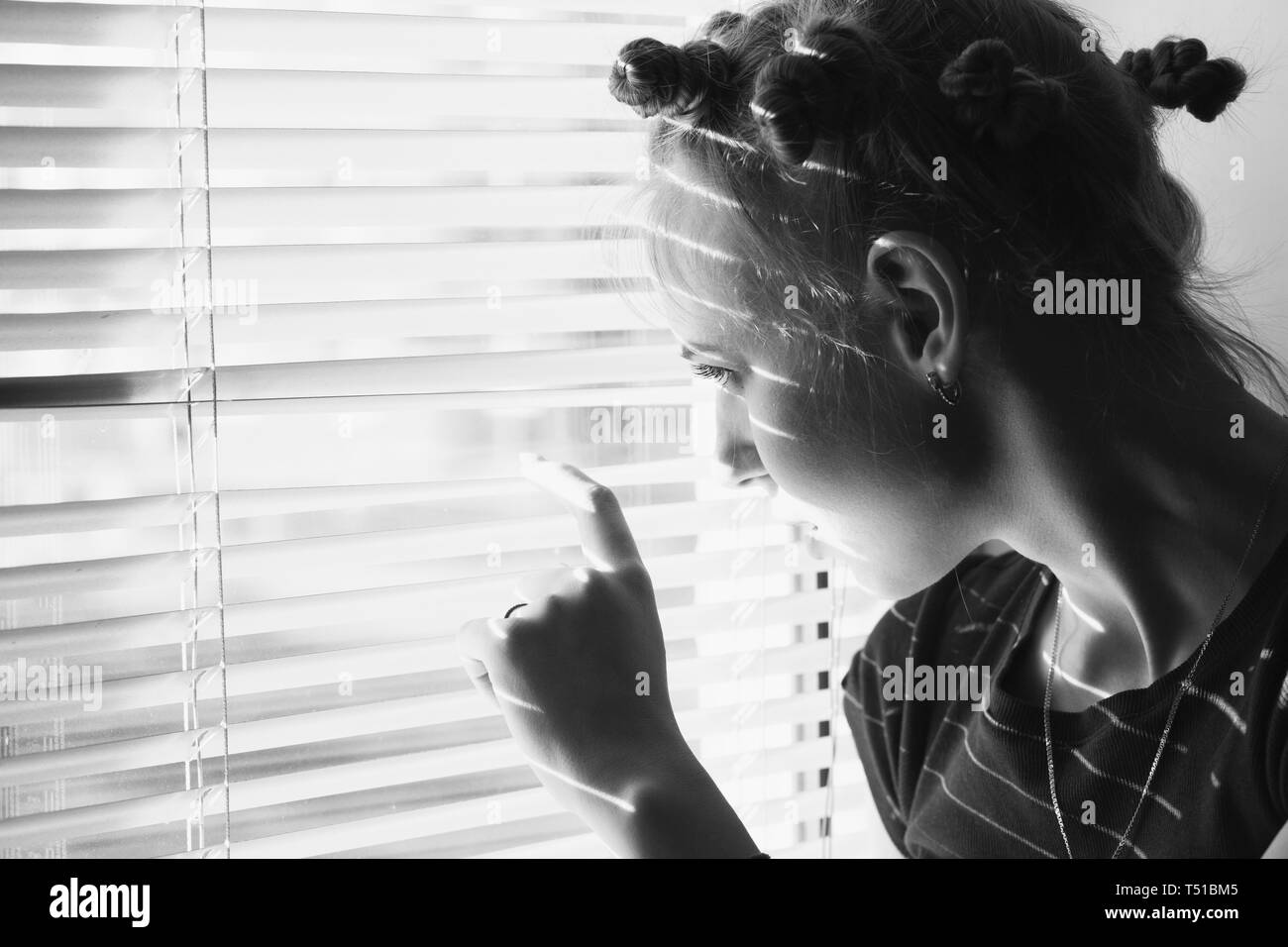 sad woman looking through blinds on window, monochrome Stock Photo