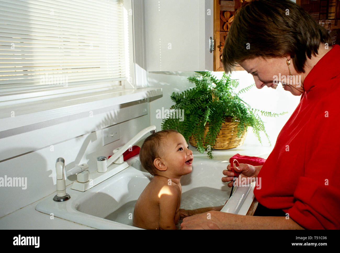 Mother bathing smiling baby in kitchen sink both laughing and bonding