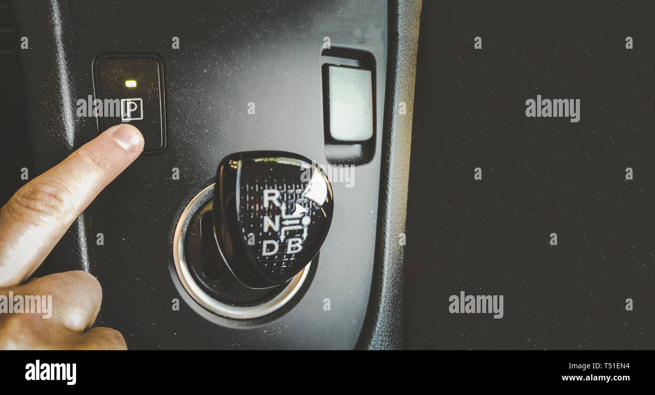 hand finger press park gear button on automatic transmission car interior overhead above view horizontal background film grain Stock Photo