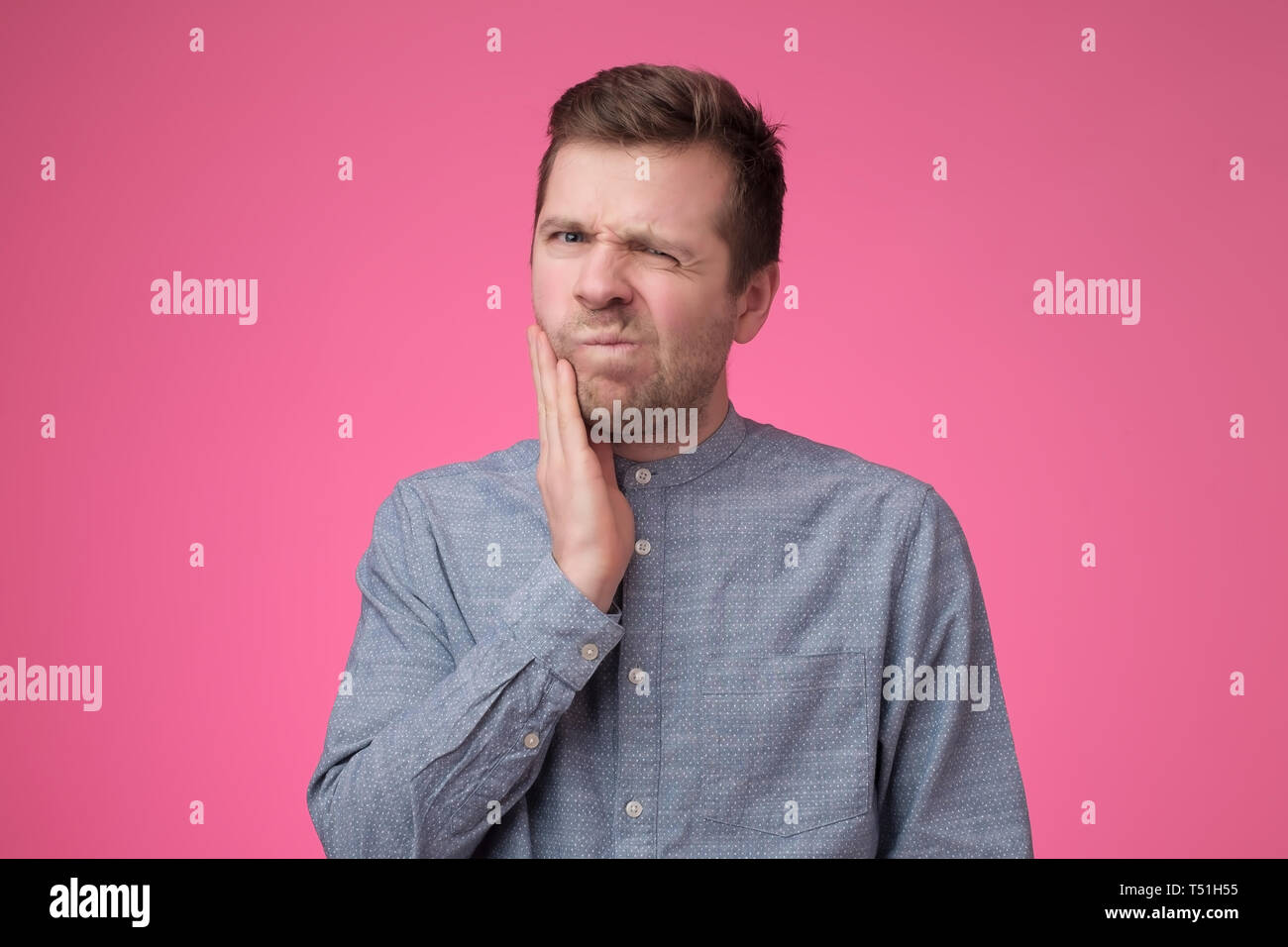 Young caucasian man is having toothache holding his cheek. Stock Photo