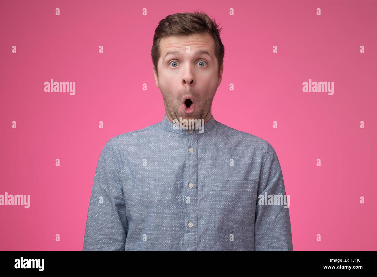Shocked face of caucasian man in blue shirt on pink background Stock Photo