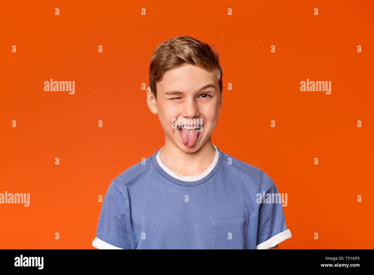 Playful teen boy winking and sticking out tongue, orange studio background Stock Photo