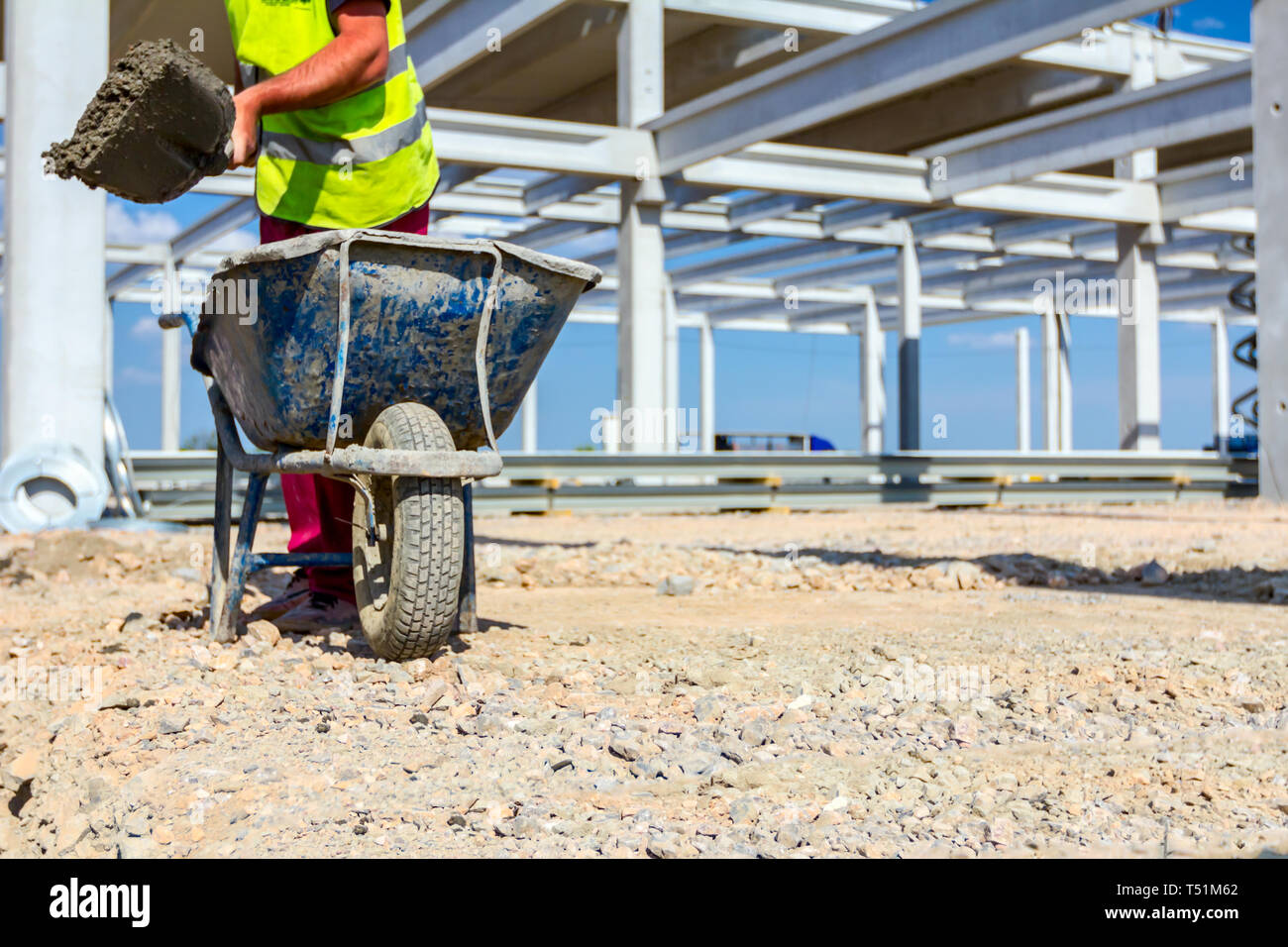 Construction worker is using shovel to unloading cement from wheelbarrow on construction site. Stock Photo