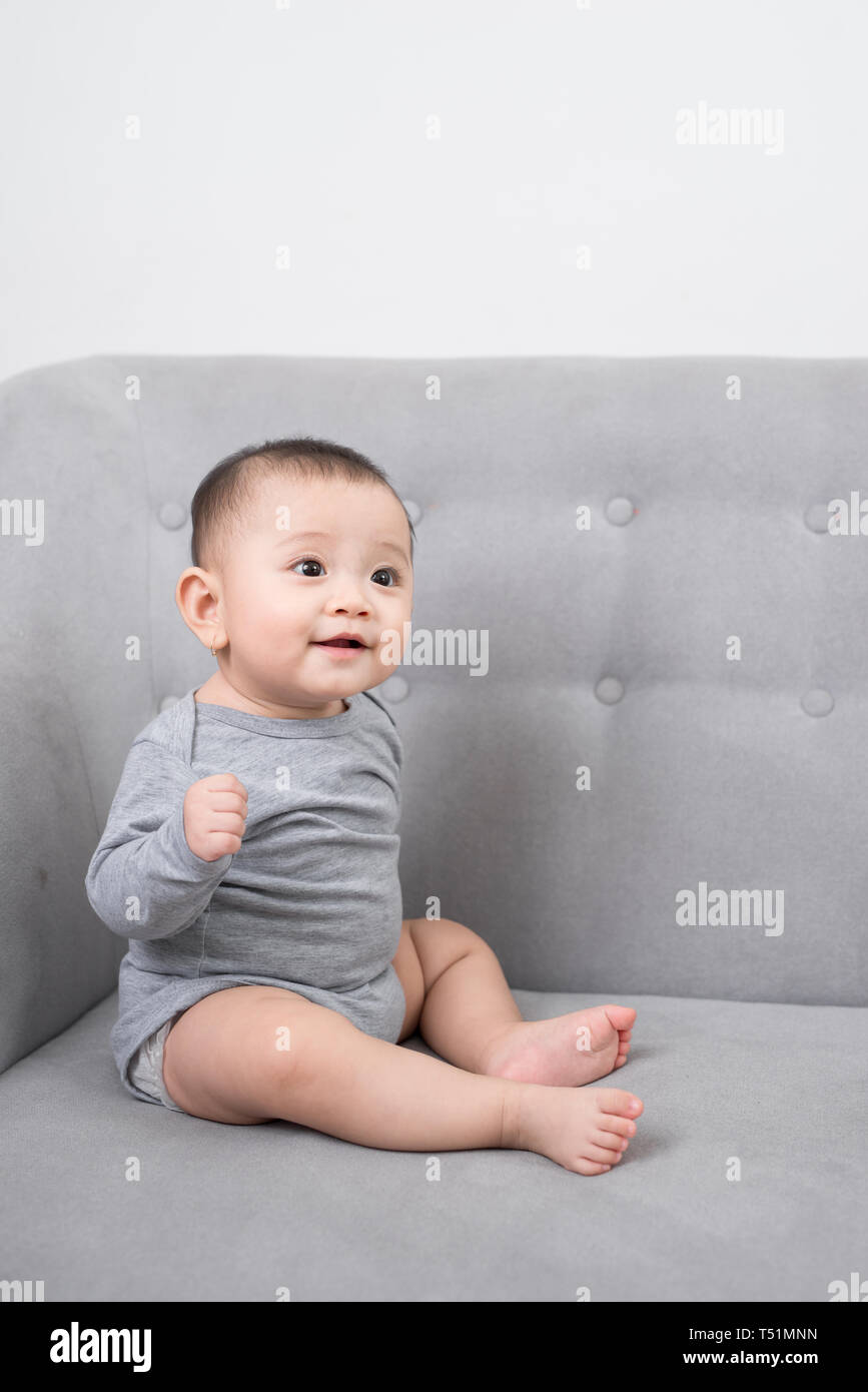 childhood, babyhood and people concept - happy little baby girl sitting on sofa at home Stock Photo