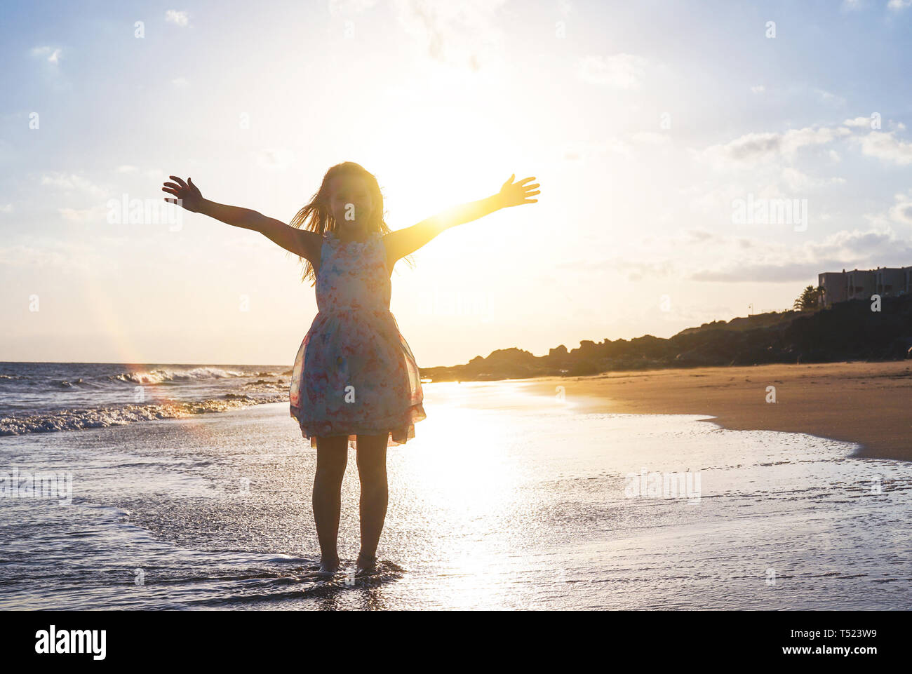 Happy child spreading her hands up on the beach on a magnificent sunset - Baby girl having fun in vacation holidays Stock Photo