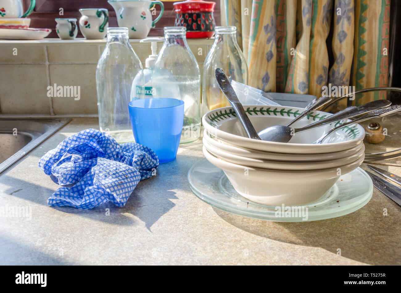 Dirty dishes and plate stacked up on a kitchen worktop next to the kitchen sink ready to wash up. Stock Photo