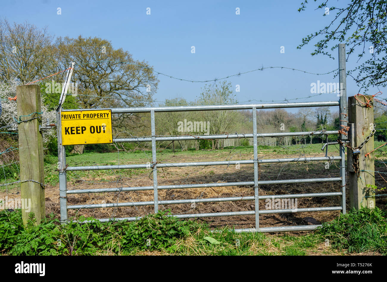 A yellow sign instructing visitors to keep out of private property is attached to a metal gate in South Staffordshire countryside near Perton village. Stock Photo