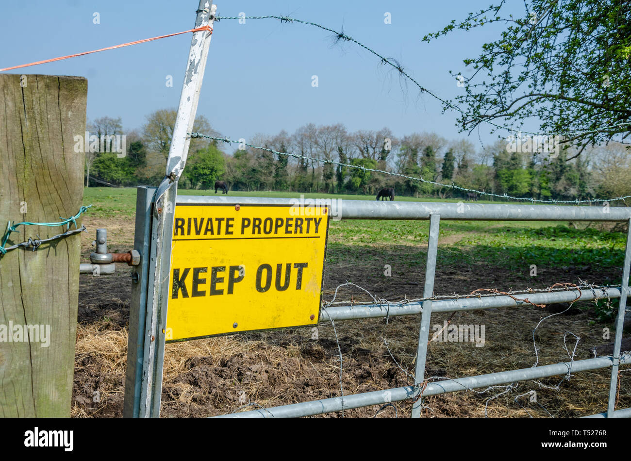 A yellow sign instructing visitors to keep out of private property is attached to a metal gate in South Staffordshire countryside near Perton village. Stock Photo