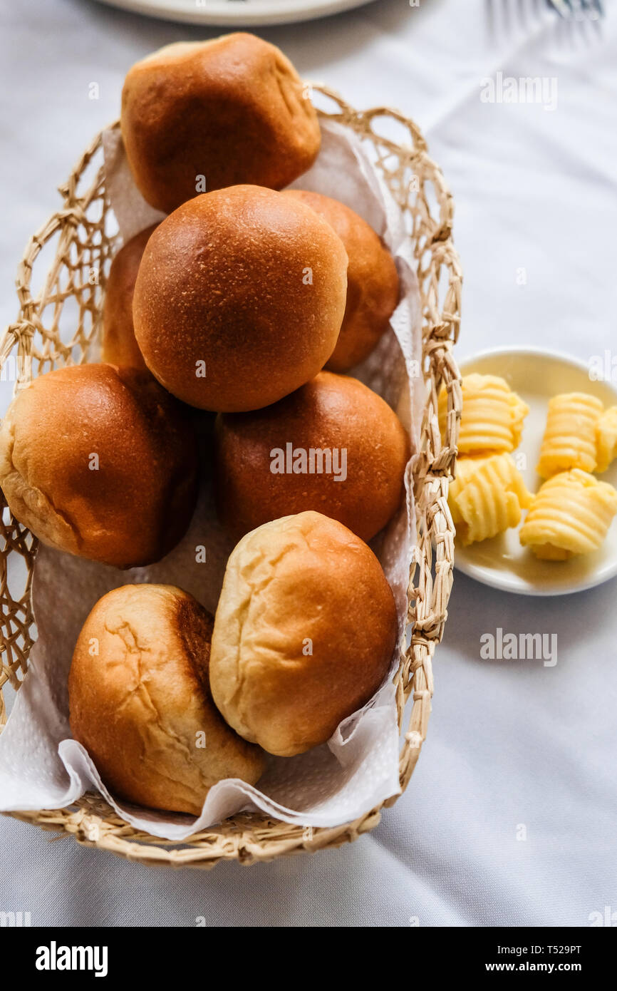 Close up of freshly baked bread rolls in basket and butter in small plate on dinning table Stock Photo