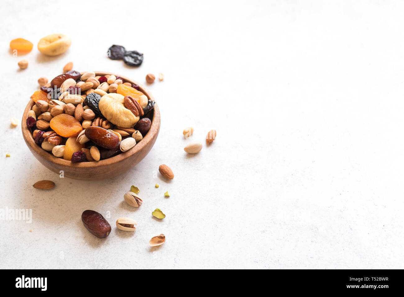Mixed nuts and dried fruits in wooden bowl on white background, copy