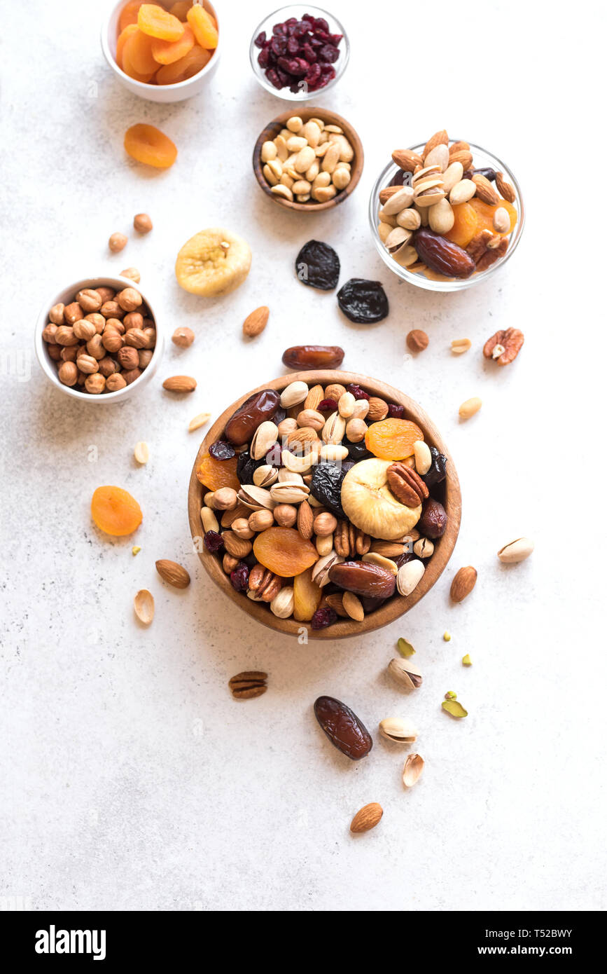 Mixed nuts and dried fruits in wooden bowl on white background, top