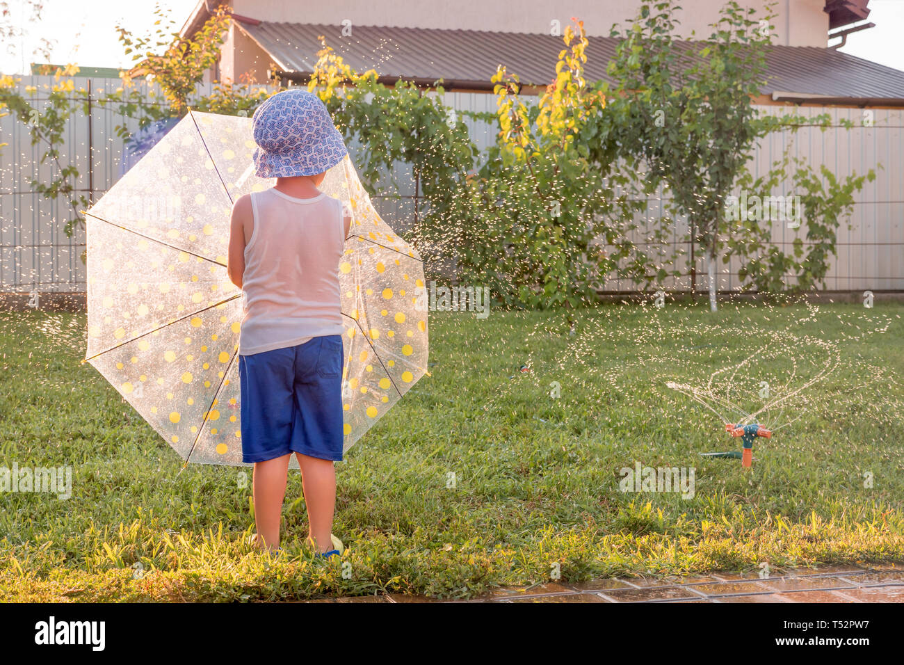 Happy childhood concept. Summer holidays with children. Automatic plant watering system. Preschooler having fun on front yard near watering system Stock Photo