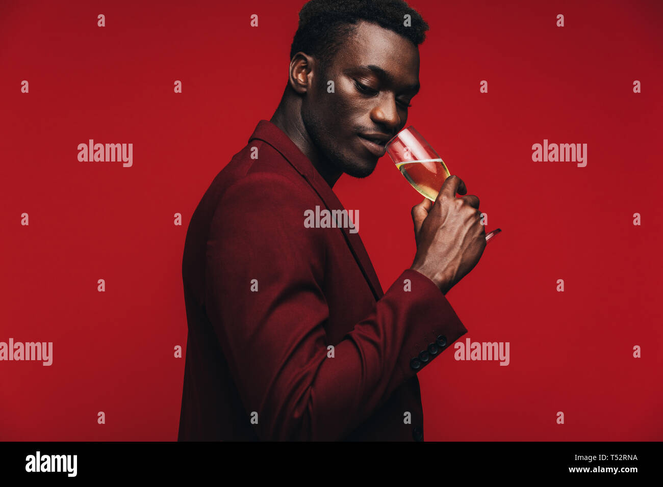 Good looking african guy drinking champagne against red background. Sophisticated african man having a glass if champagne. Stock Photo