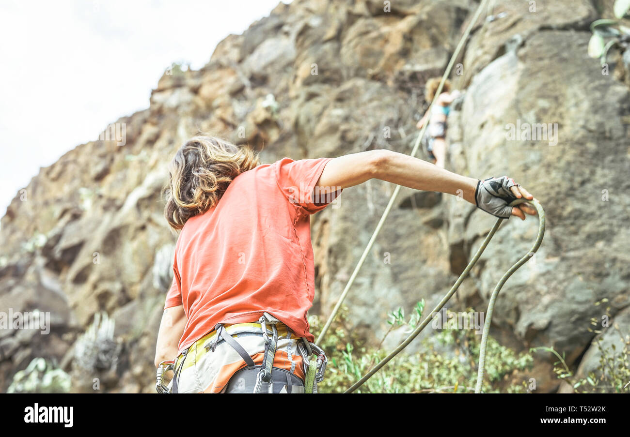 Man giving security to woman who is climbing up on mountain cliff - Climber in action on the rock near the peak Stock Photo