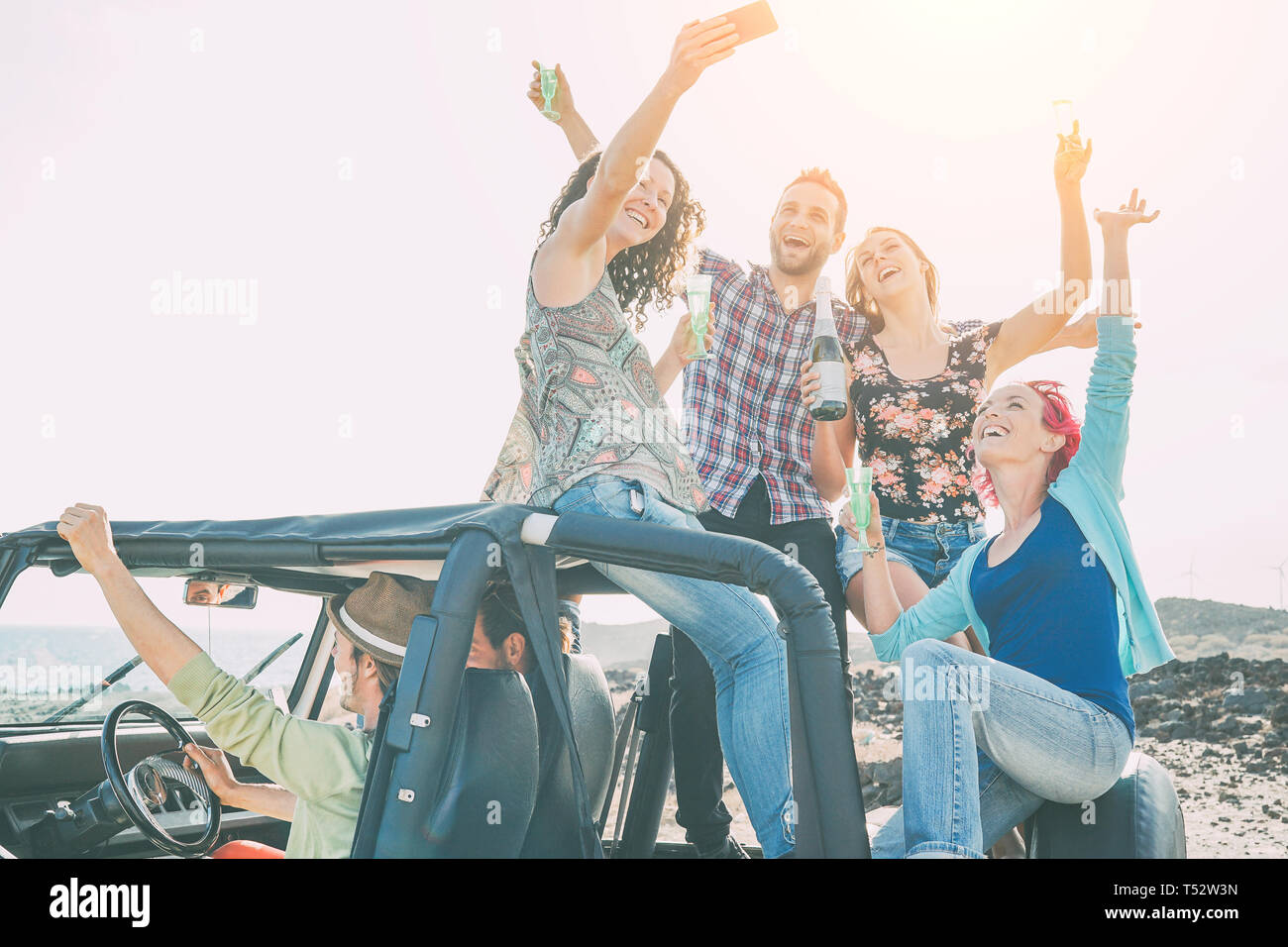 Group of happy friends making party on a jeep car - Young people having fun drinking champagne and taking photo selfie during their road trip Stock Photo