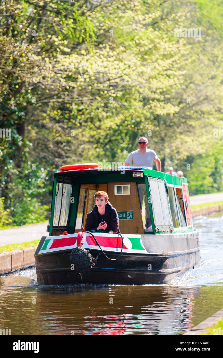 Front view of a narrow boat moving along the Shropshire Union Canal, UK. Canal boat and people back lit on a sunny spring day. Stock Photo