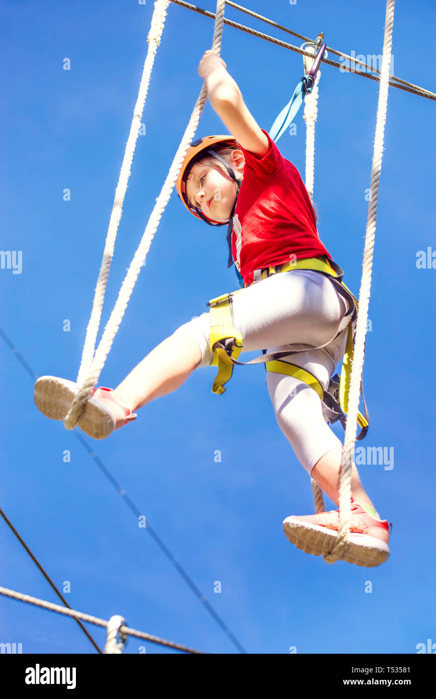 Little brave caucasian girl at outdoor treetop climbing adventure park Stock Photo