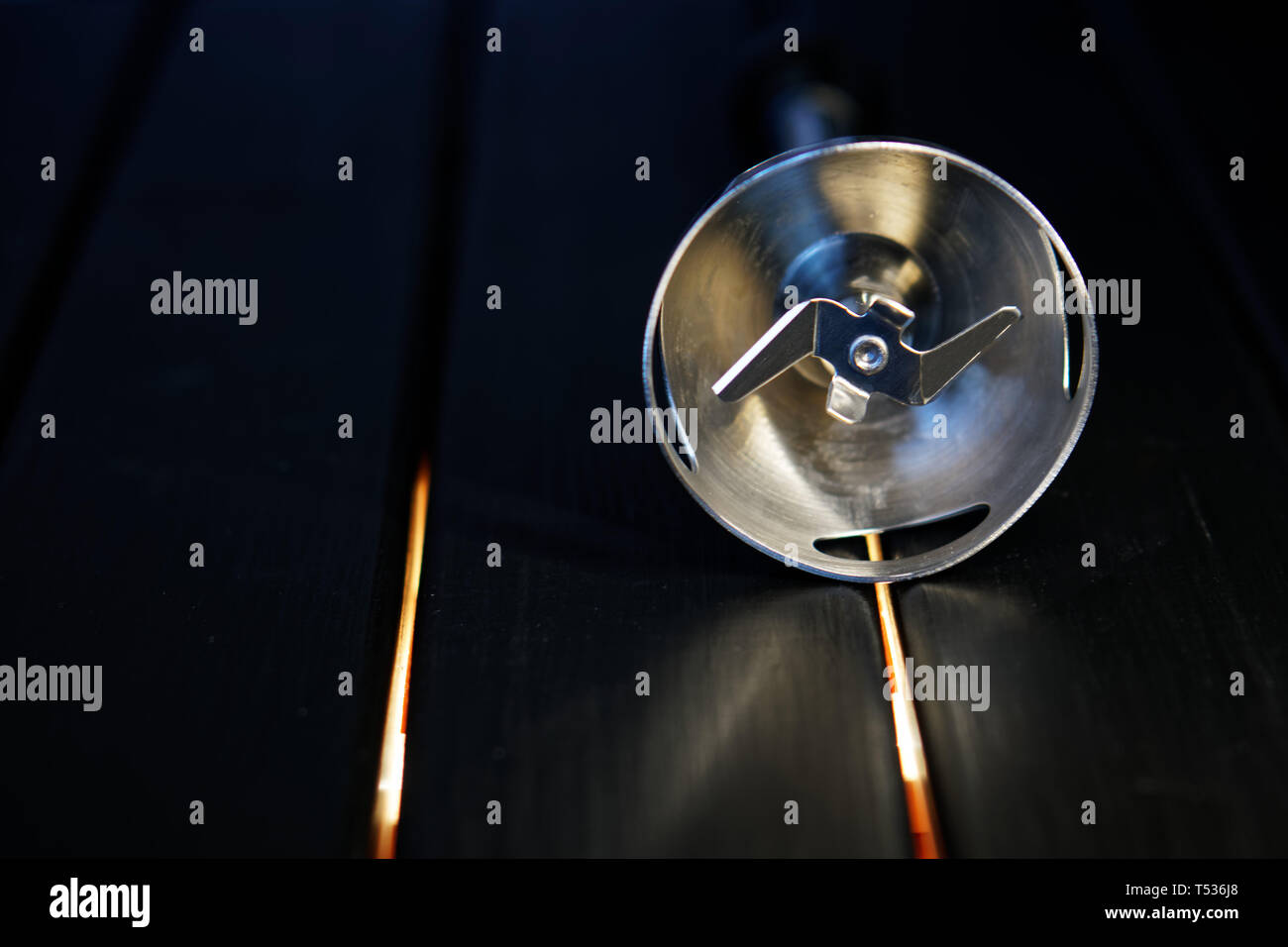 Rotating knife nozzle for blender lies on a black wooden surface. Device for cooking. Close-up Stock Photo
