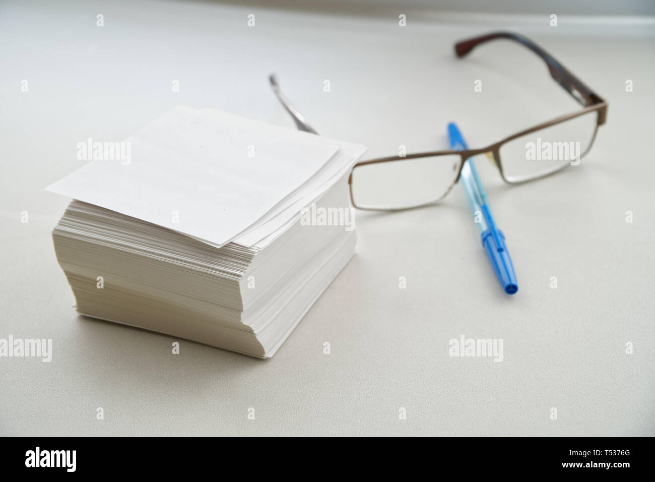 A stack of sheets for records, glasses and a fountain pen are on a white table by the window in the office. Work on cataloging. Close-up Stock Photo