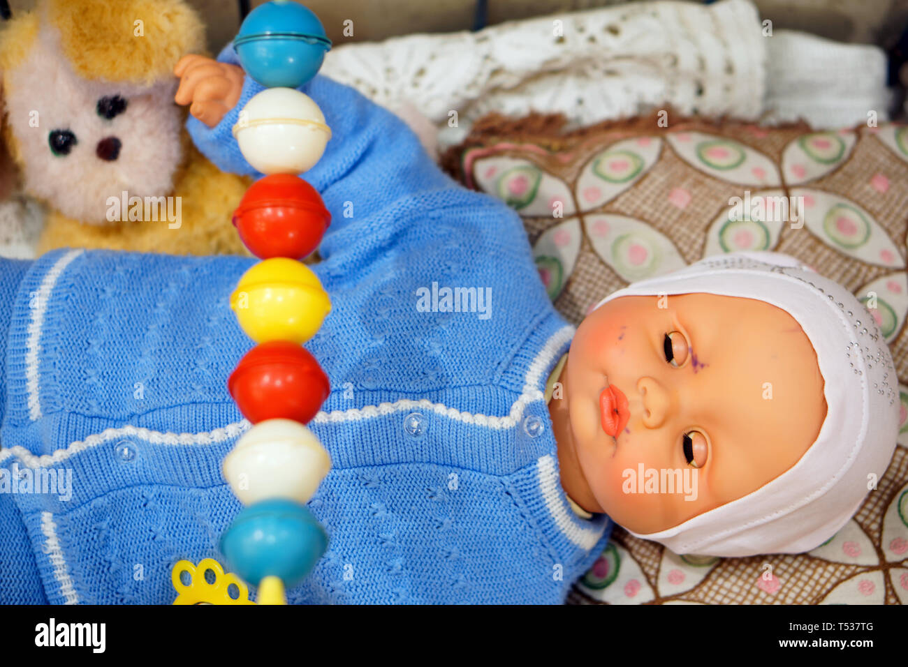 Old toy, vintage doll - baby in a blue sweater in a crib with a dog. Subject from the past. Stock Photo