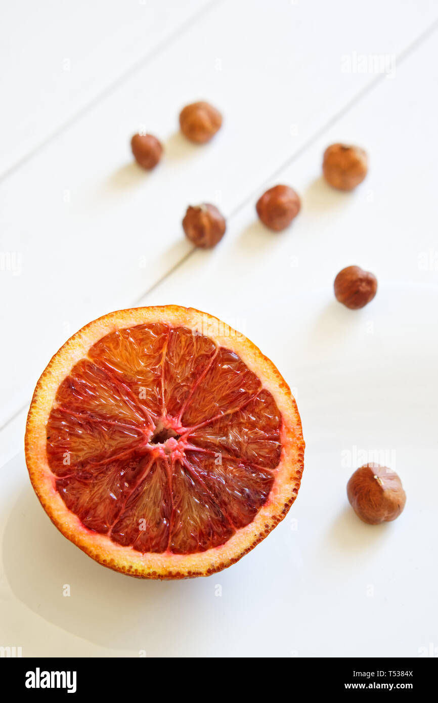 Red orange and hazelnuts on the white diagonal surface from painted boards. Daylight. Vertical picture Stock Photo