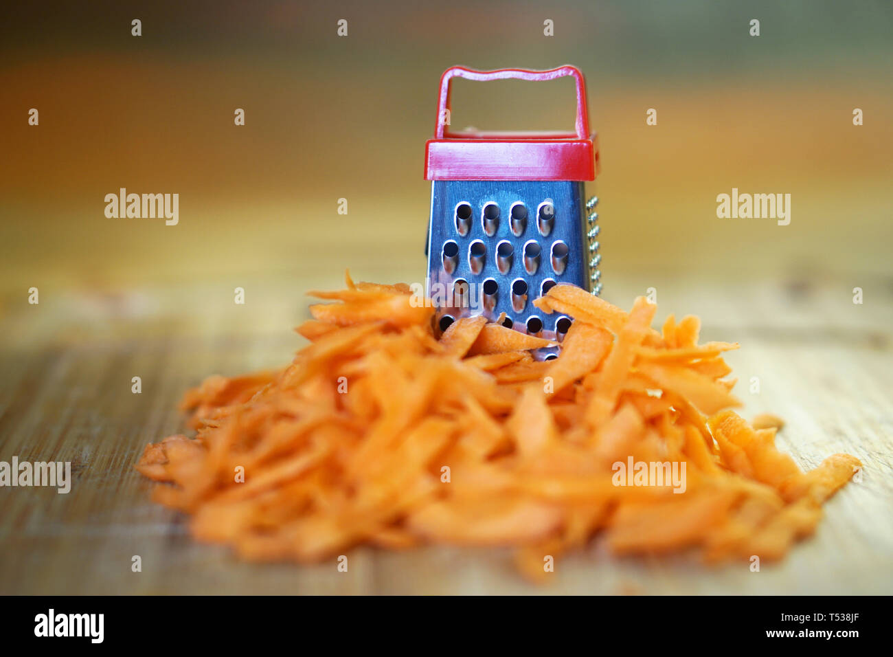 A large carrot and a small grater on a cutting board in the kitchen. Optical illusion. Close-up. Shallow depth of field. Horizontal image. Stock Photo