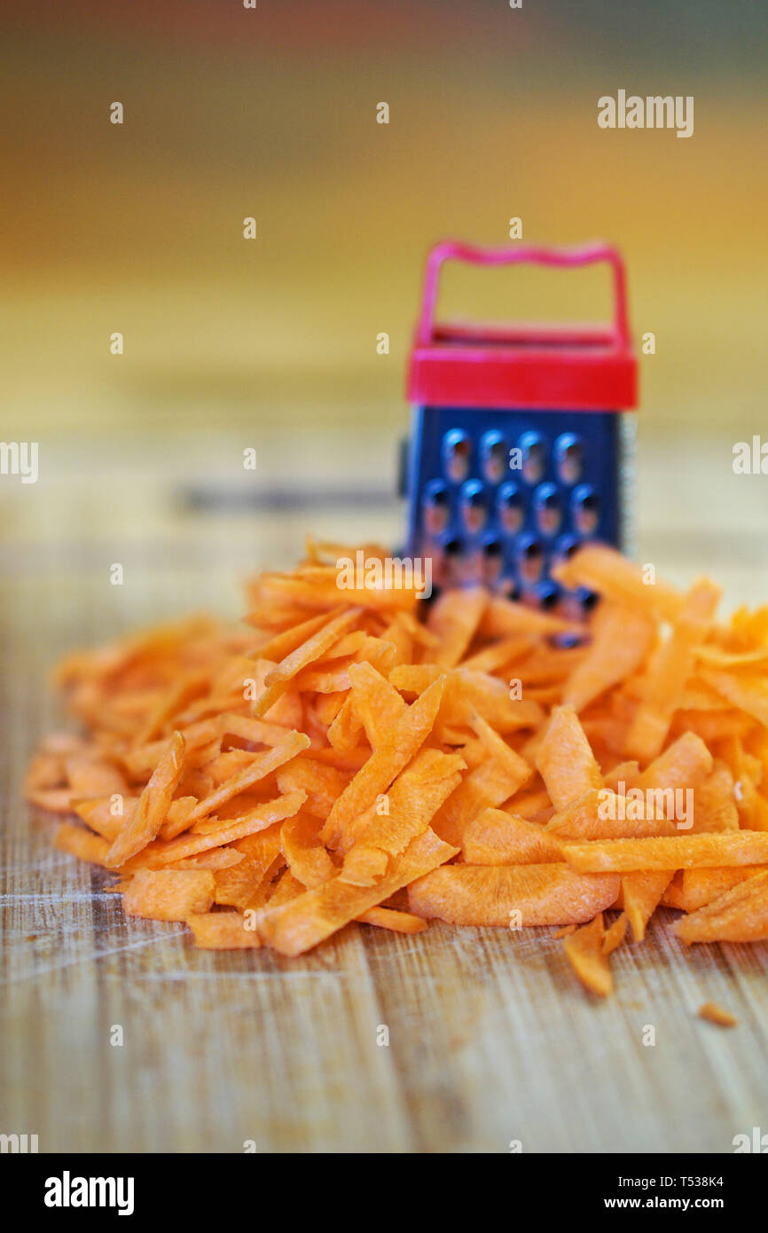 A small grater and a large carrot on a cutting board, in the kitchen. Optical illusion. Close-up. Shallow depth of field. Vertical image Stock Photo