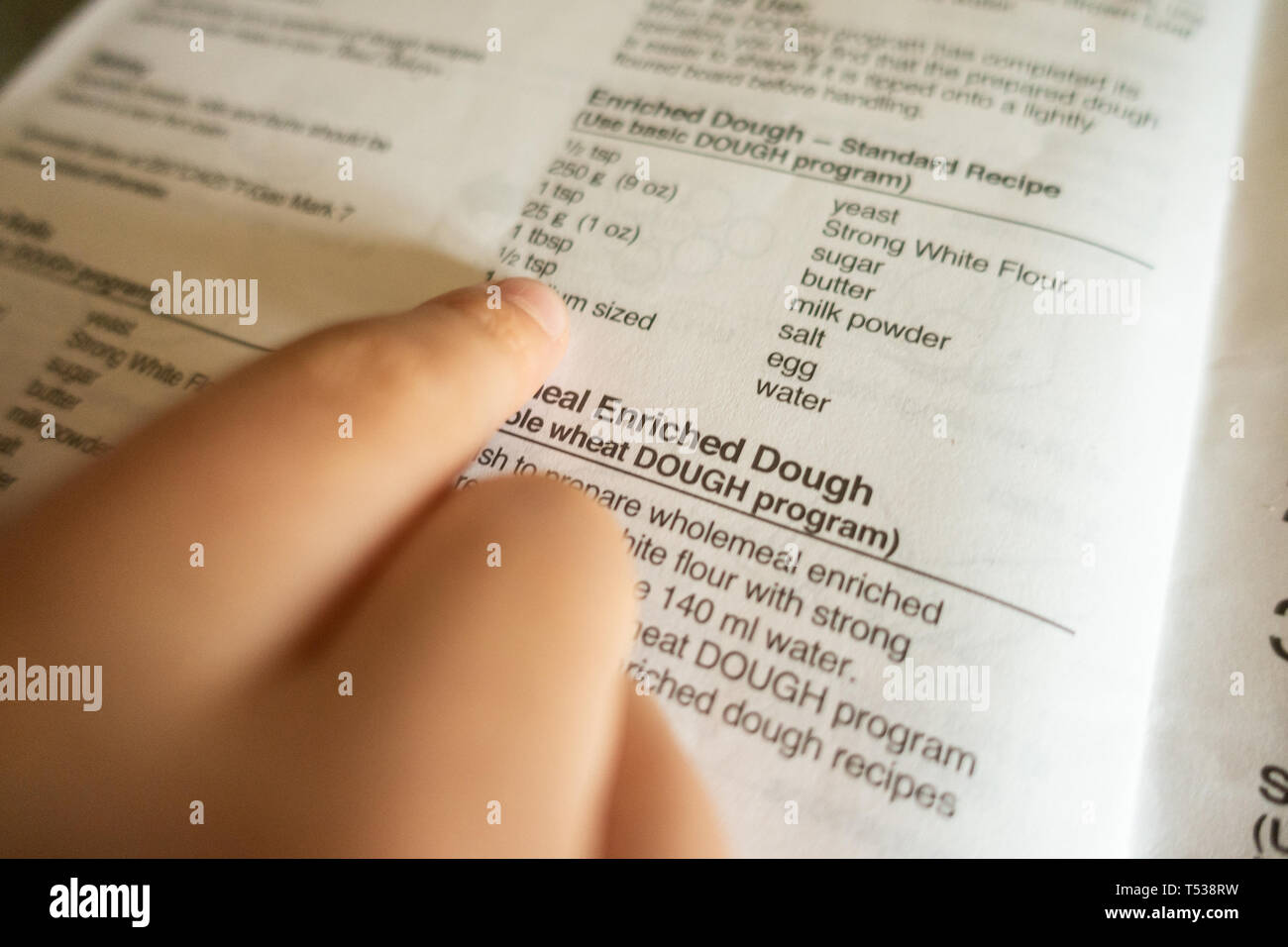 A child follows recipe in a cookery book and uses his finger to follow the words as he reads. Stock Photo