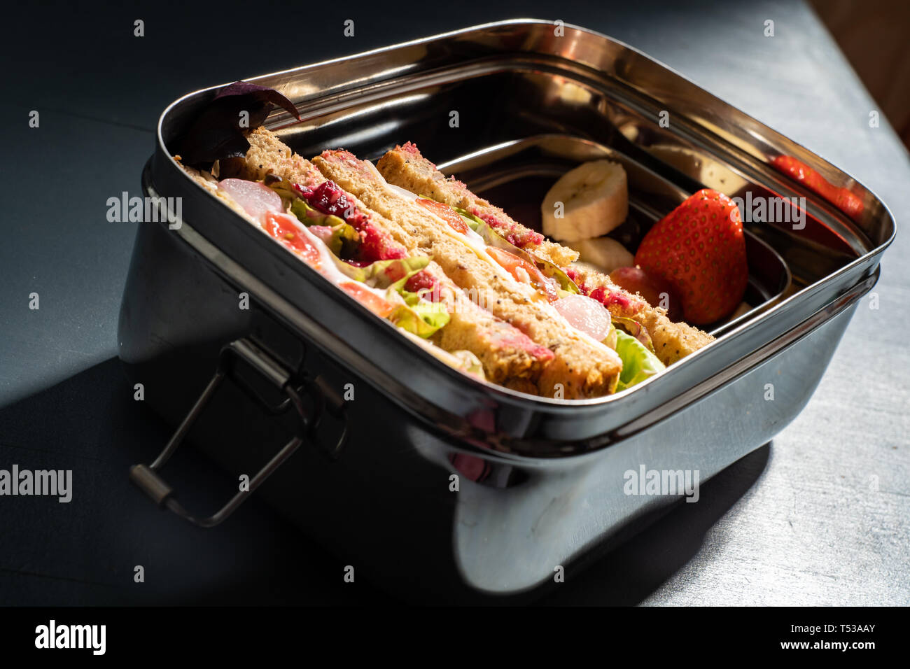 Healthy sandwiches on brown seeded bread and mixed fruit snacks in a stainless steel lunch box with compartments. Re-usable stainless steel means no p Stock Photo
