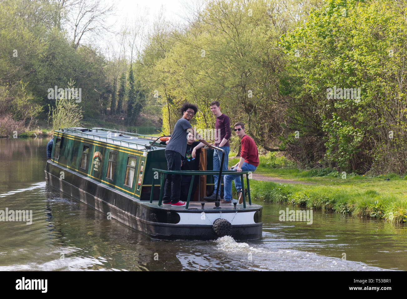 Group of British lads out together in narrowboat travelling along UK canal. Boating holiday in spring sunshine. Having fun in the sun. Staycation UK. Stock Photo
