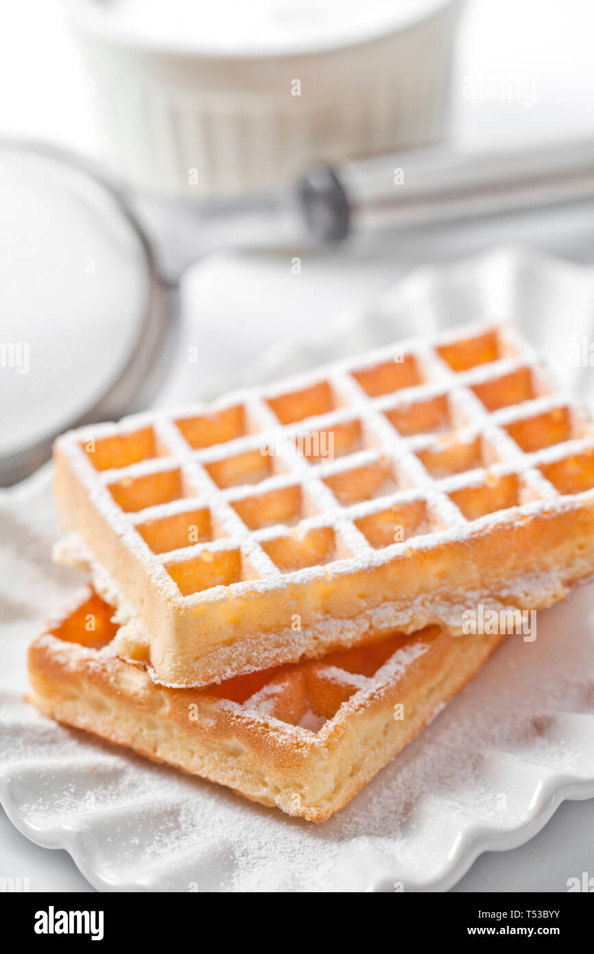 Belgium waffers with sugar powder on ceramic plate and strainer on ...
