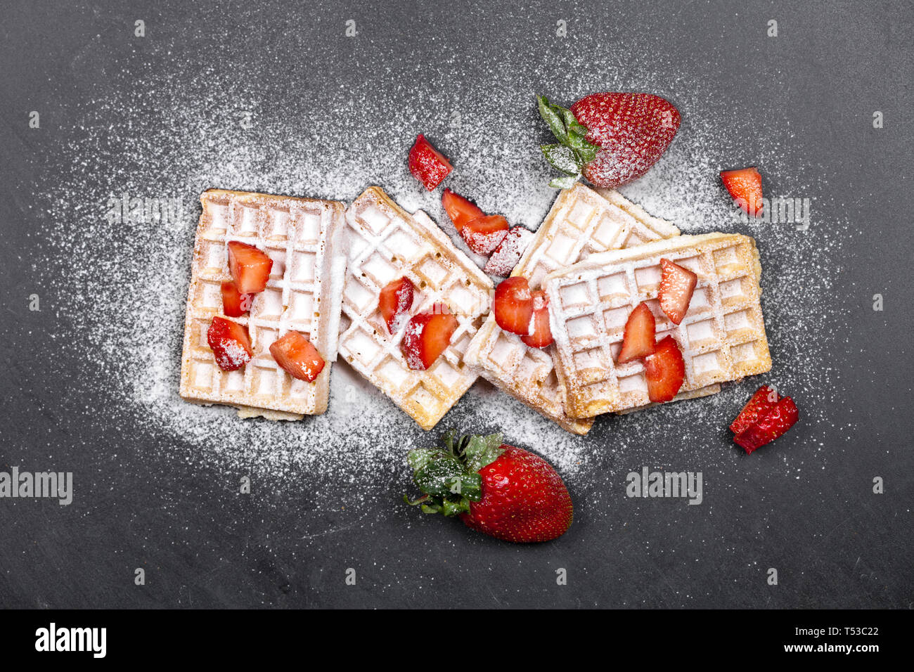 Belgium waffers with strawberries and sugar powder on black board ...