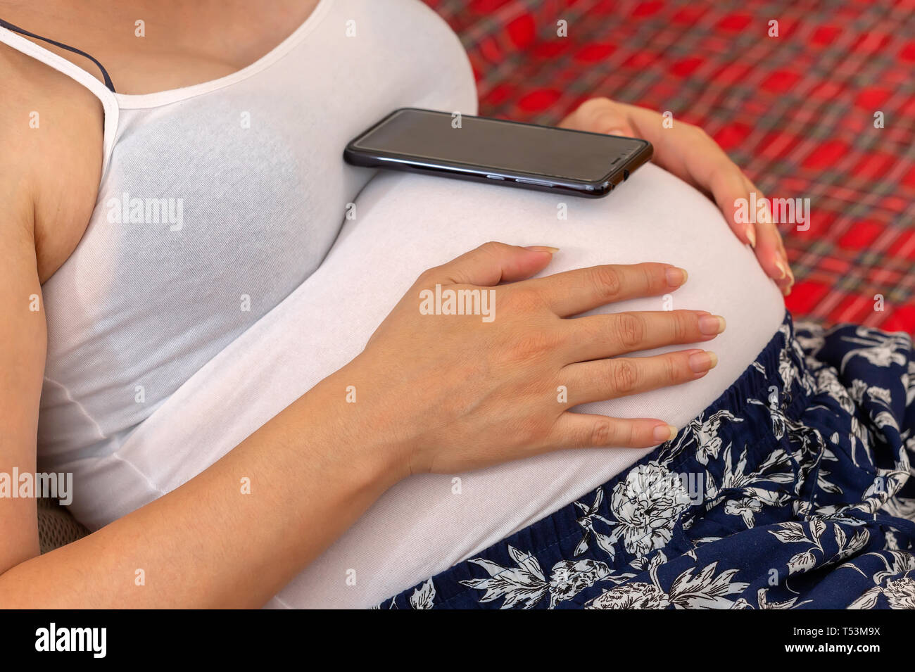 Pregnant woman using cell phone on her belly. Waiting for that important call. Stock Photo