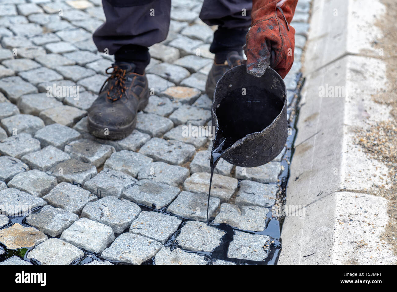Pouring molten pitch from a tar bucket. Traditional pitch jointing for paved driveway. Worker