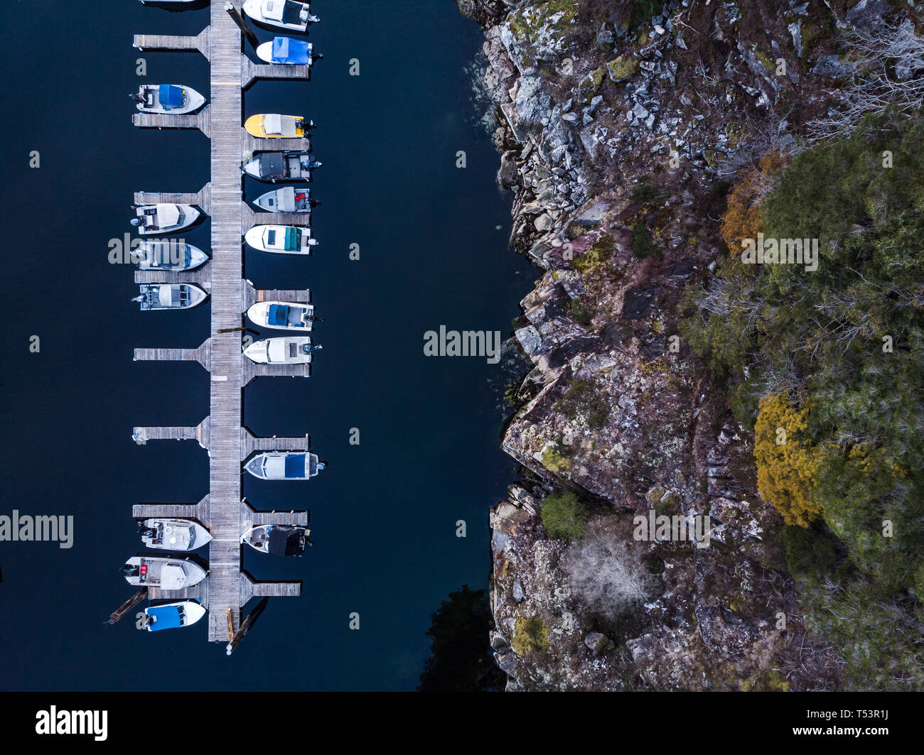 Aerial overhead view of a wooden boat dock next to a rocky seaside cliff Stock Photo