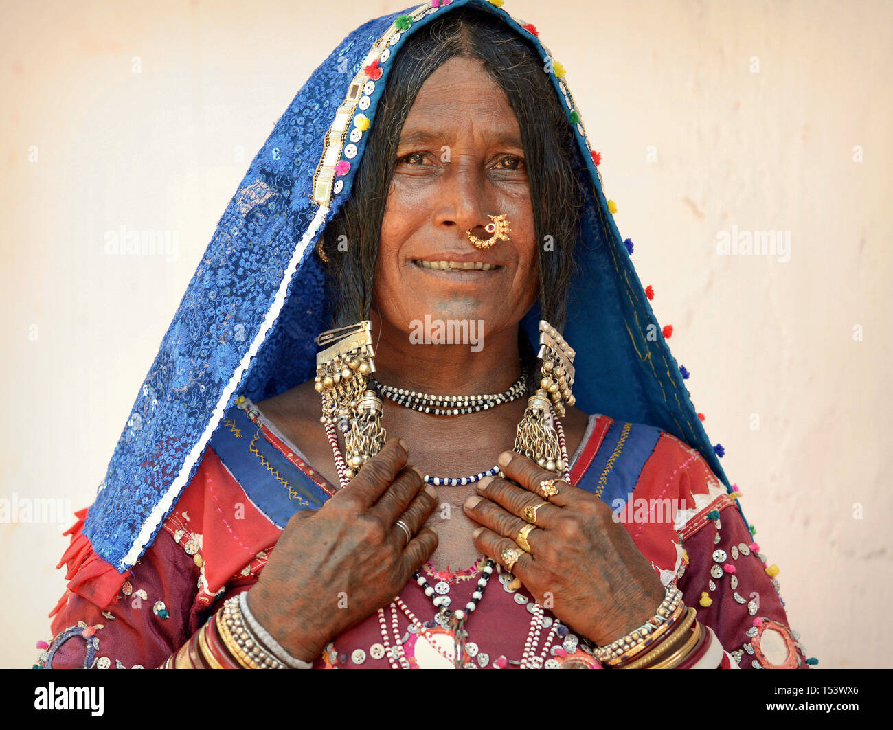 Elderly Indian Lambadi woman (Banjara, Indian gypsy) from Karnataka poses in her traditional outfit for the camera and shows her silver jewelry. Stock Photo