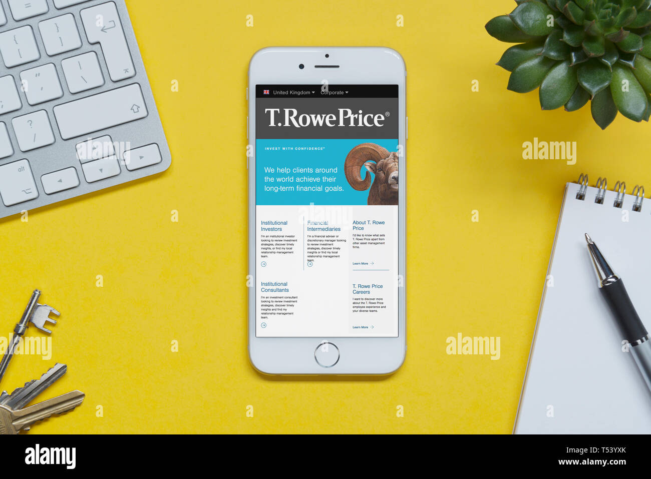 An iPhone showing the T. Rowe Price website rests on a yellow background table with a keyboard, keys, notepad and plant (Editorial use only). Stock Photo