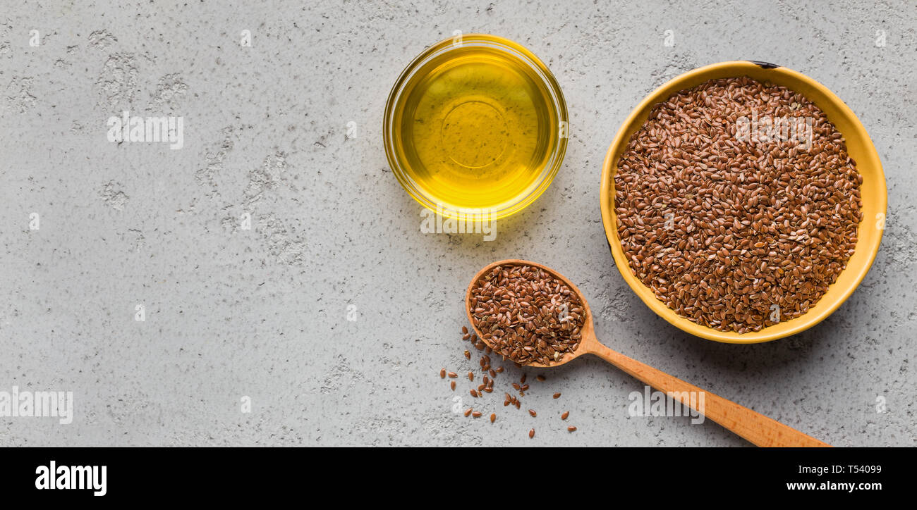 Linseed oil, bowl and spoon of linseeds on concrete background, top