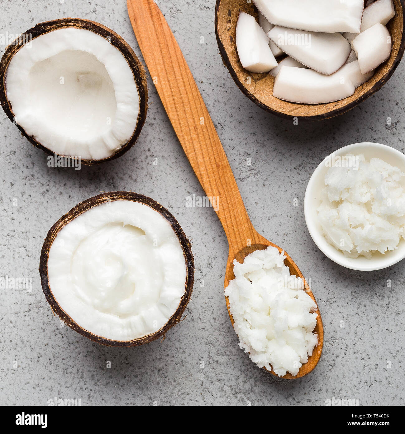 Coconut butter in bowl and spoon, coconut pieces in coco shell on concrete background, top view. Super food concept Stock Photo
