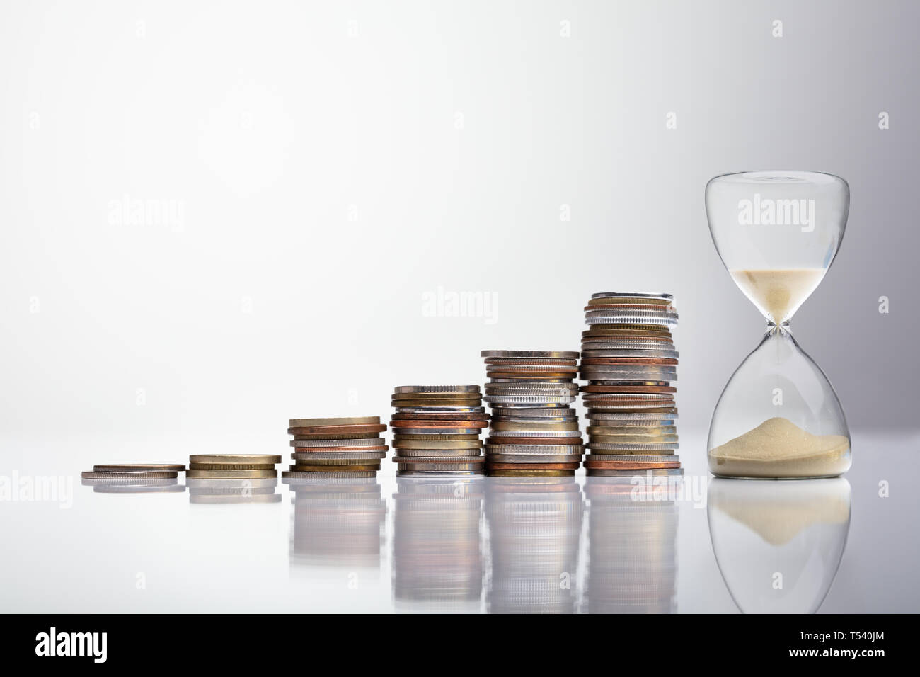 Close-up Of Hourglass Near Stack Of Coins Over Desk Stock Photo