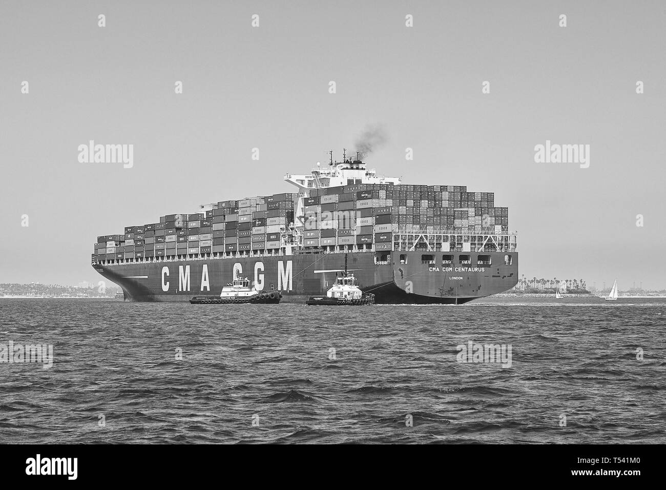 Black And White Photo Of Container Ship, CMA CGM CENTAURUS, Being Turned Through 180 Degrees By 2 Tugs Before Docking In Long Beach, California. USA. Stock Photo