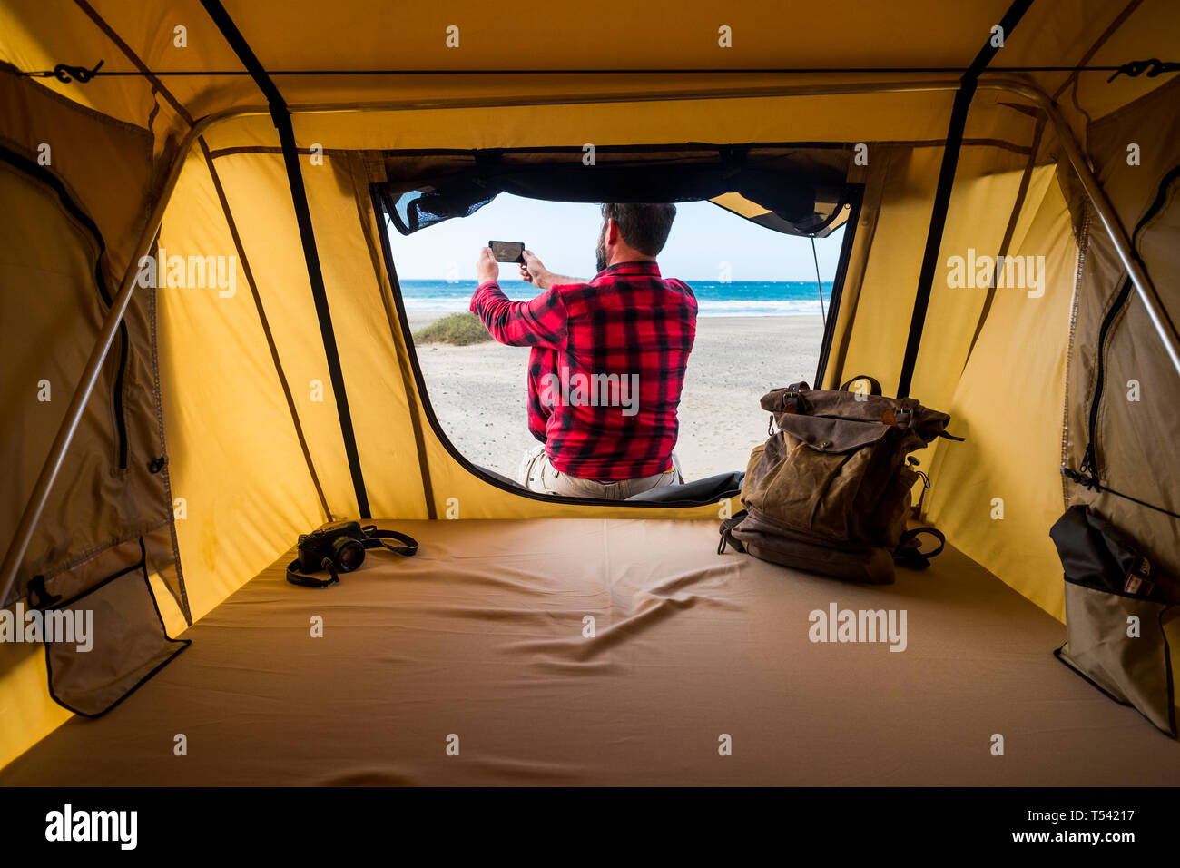 Freedom traveler man outside the tent in alternative vacation lifestyle in free camping at the beach taking picture of the natura landscape - backpack Stock Photo
