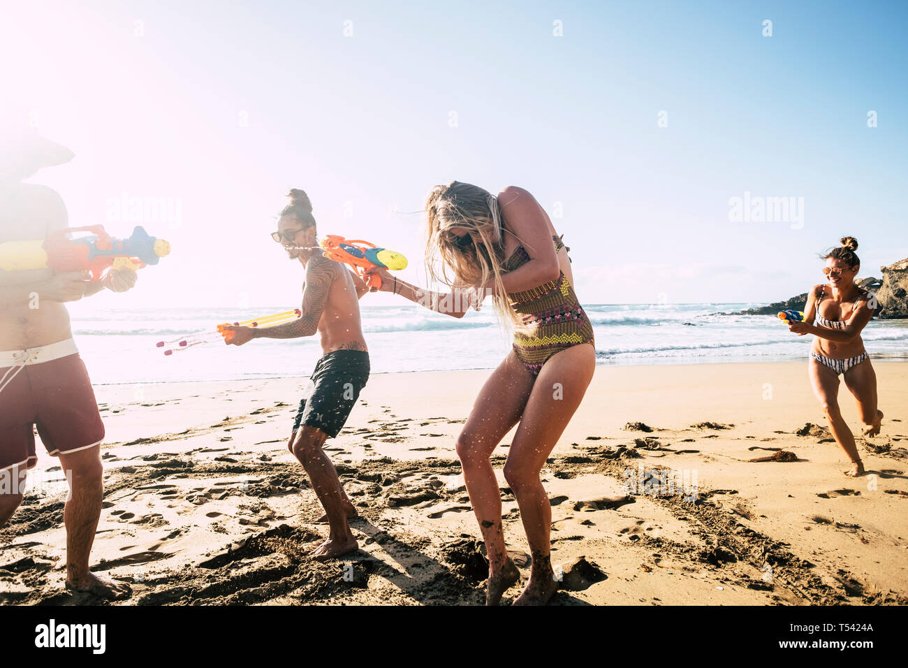 People having fun together in friendship at the beach playing with water guns in bikini under the hot summer sun - craziness and friends - bright imag Stock Photo