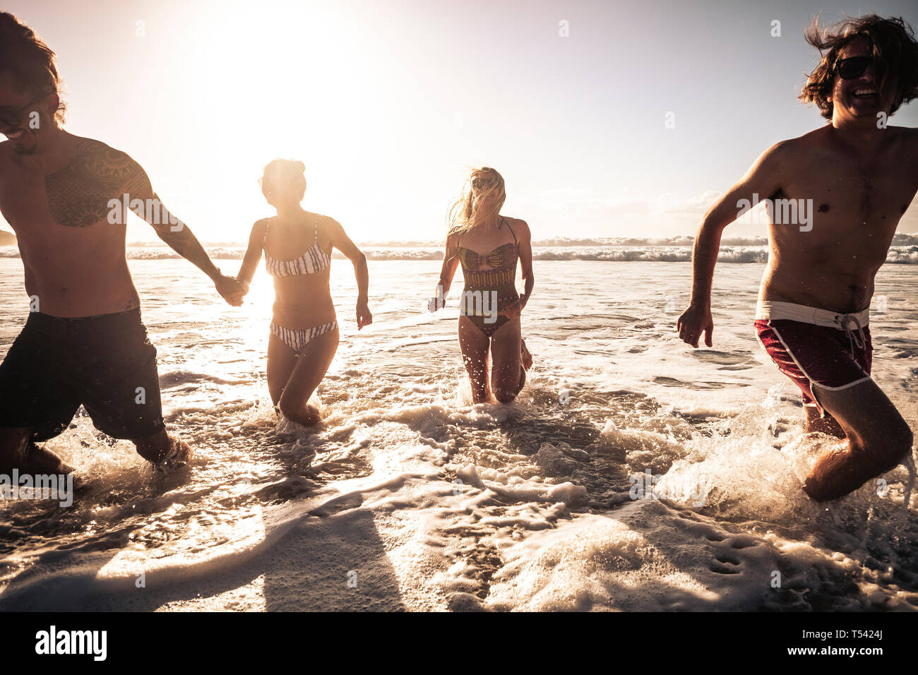 Group of beautiful millennial alternative young people have fun and enjoy the summer holiday vacation together in friendship running in the water of t Stock Photo