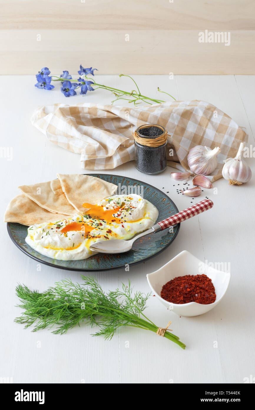 Dish with Turkish eggs Cilbir, plain yogurt, poached eggs, garlic, chilli, fresh dill and melted butter. Embellished with few pieces of lavash bread a Stock Photo