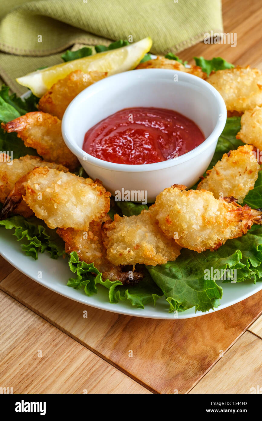 Breaded and fried butterfly coconut shrimp served on bed of romaine lettuce with spicy cocktail dipping sauce Stock Photo