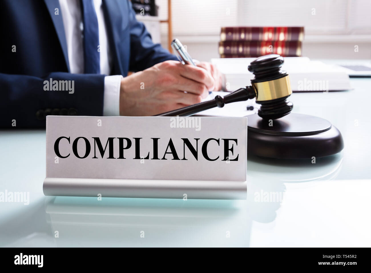 Compliance Name Plate Over Reflected Desk Near Gavel And Justice In Courtroom Stock Photo