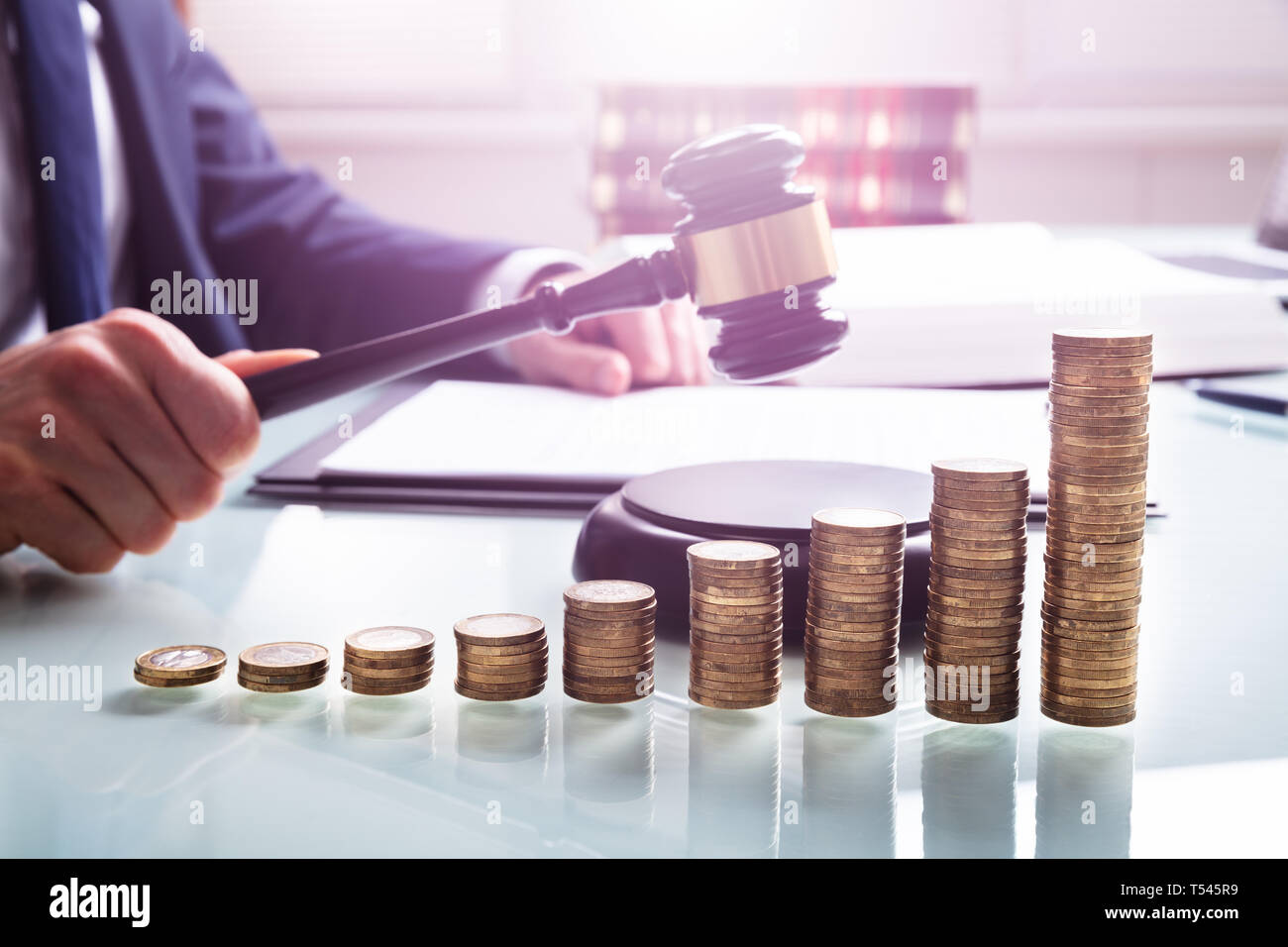 Close-up Of Judge Hand Hitting Mallet On Sound Block In Front Of Stacked Coins Stock Photo
