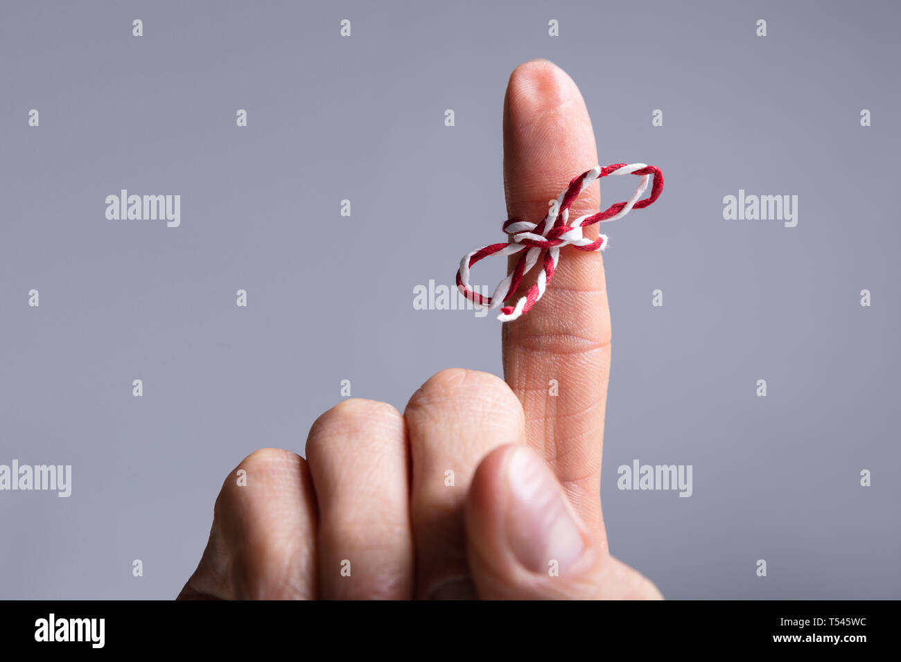 Close-up Of Person's Finger With Tied Ribbon Bow Over Gray Background Stock Photo
