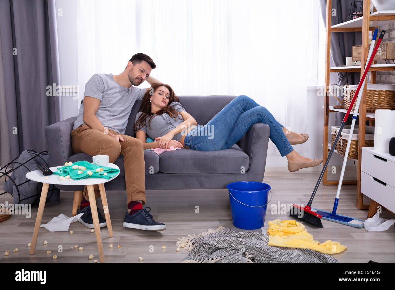 Smiling Couple Relaxing On Sofa In Messy Living Room At Home Stock Photo